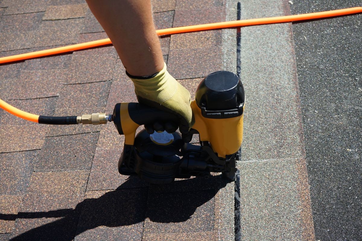 New roof shingle being applied. A Roofer nailing asphalt shingles with air gun.